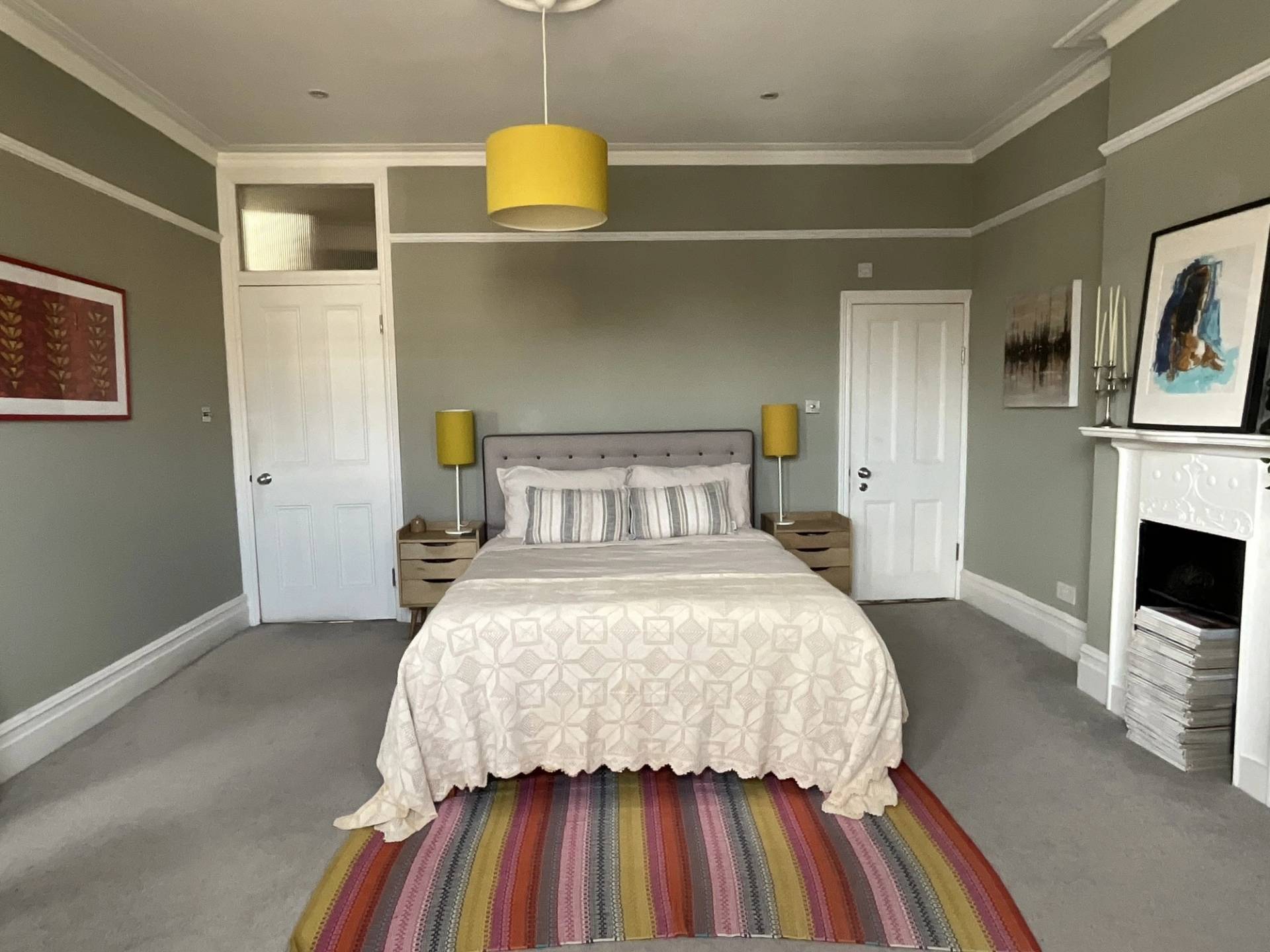 Spacious olive green master bedroom suite with yellow pendant lamp, beige bedspread, and colorful striped area rug, Love Locations.