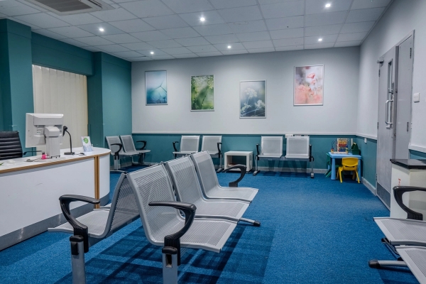 Hospital waiting area featuring silver metal beam seating, blue carpets, and framed wall art, Love Locations UB4.