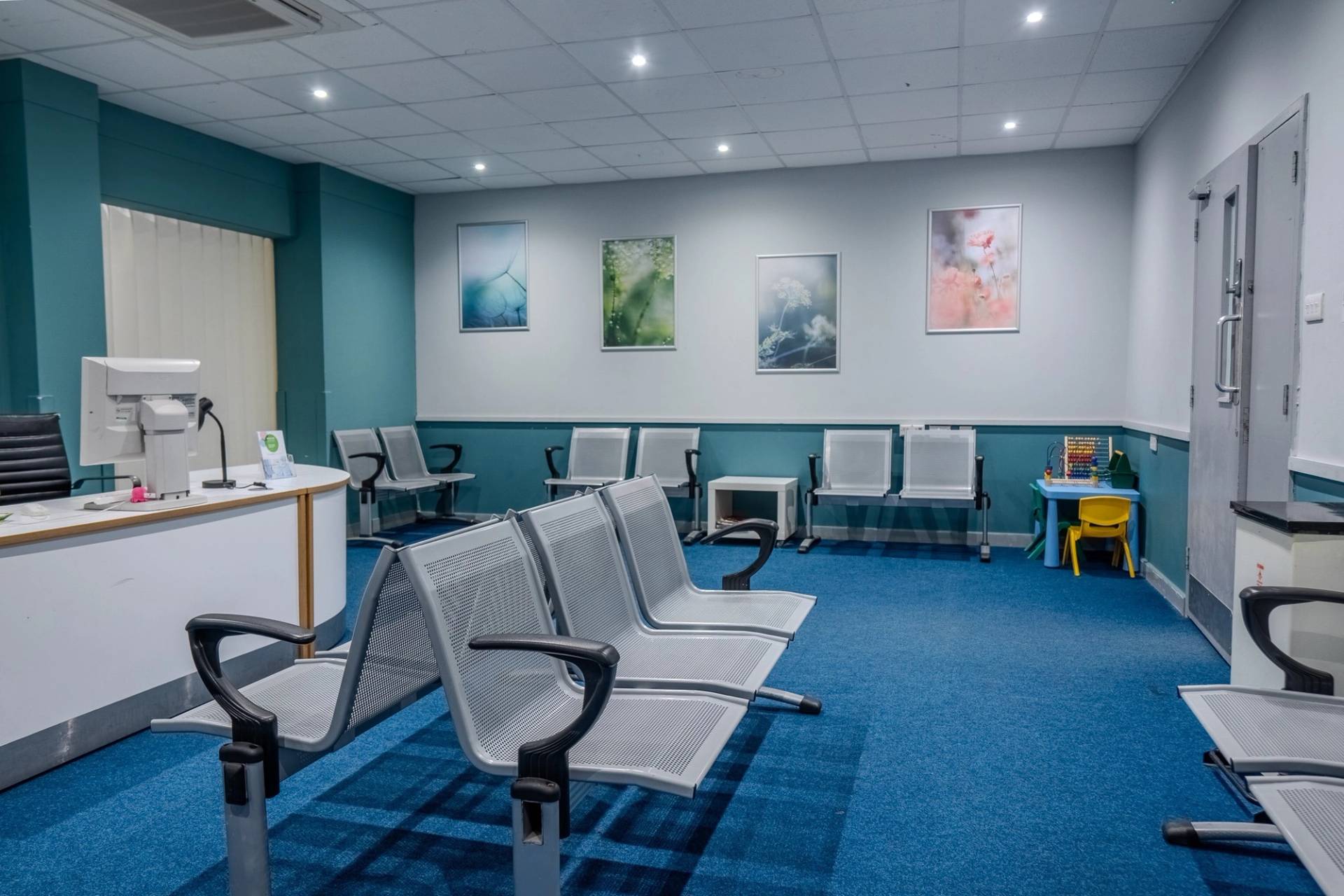 Hospital waiting area featuring silver metal beam seating, blue carpets, and framed wall art, Love Locations UB4.