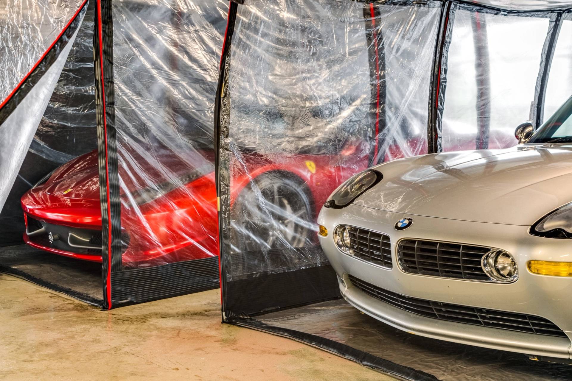 Close-up detail of silver and red luxury sports cars in protective clear storage pods via Love Locations.