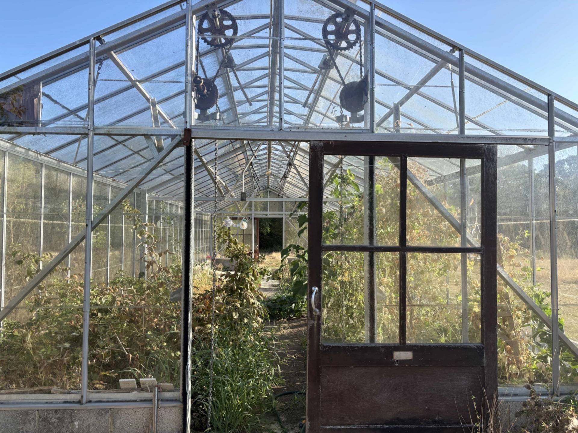 Industrial greenhouse frame interior view with pulley gear mechanisms and open sliding doors, Love Locations BN8.