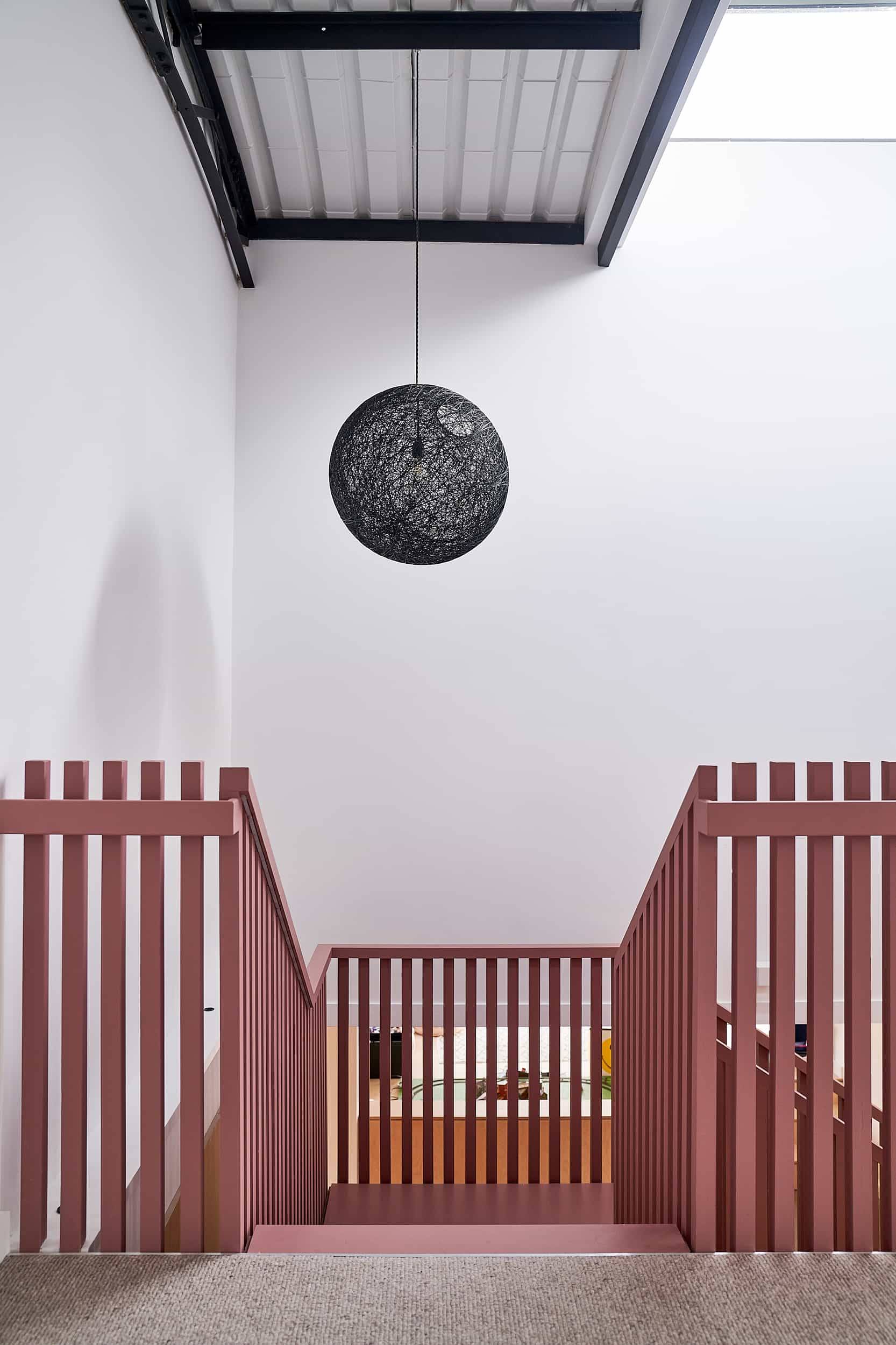 Architectural terracotta pink slatted balcony landing looking up toward a dark circular pendant light, Love Locations IP30.