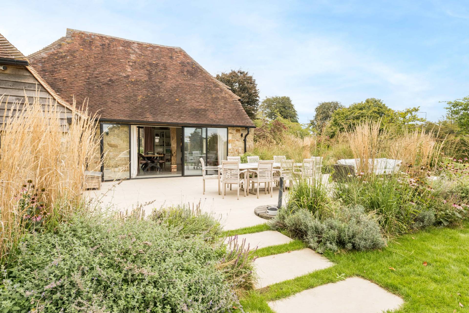 Paved stone patio terrace set beside a converted barn facade with lavender and shrub garden borders, Love Locations GU28.