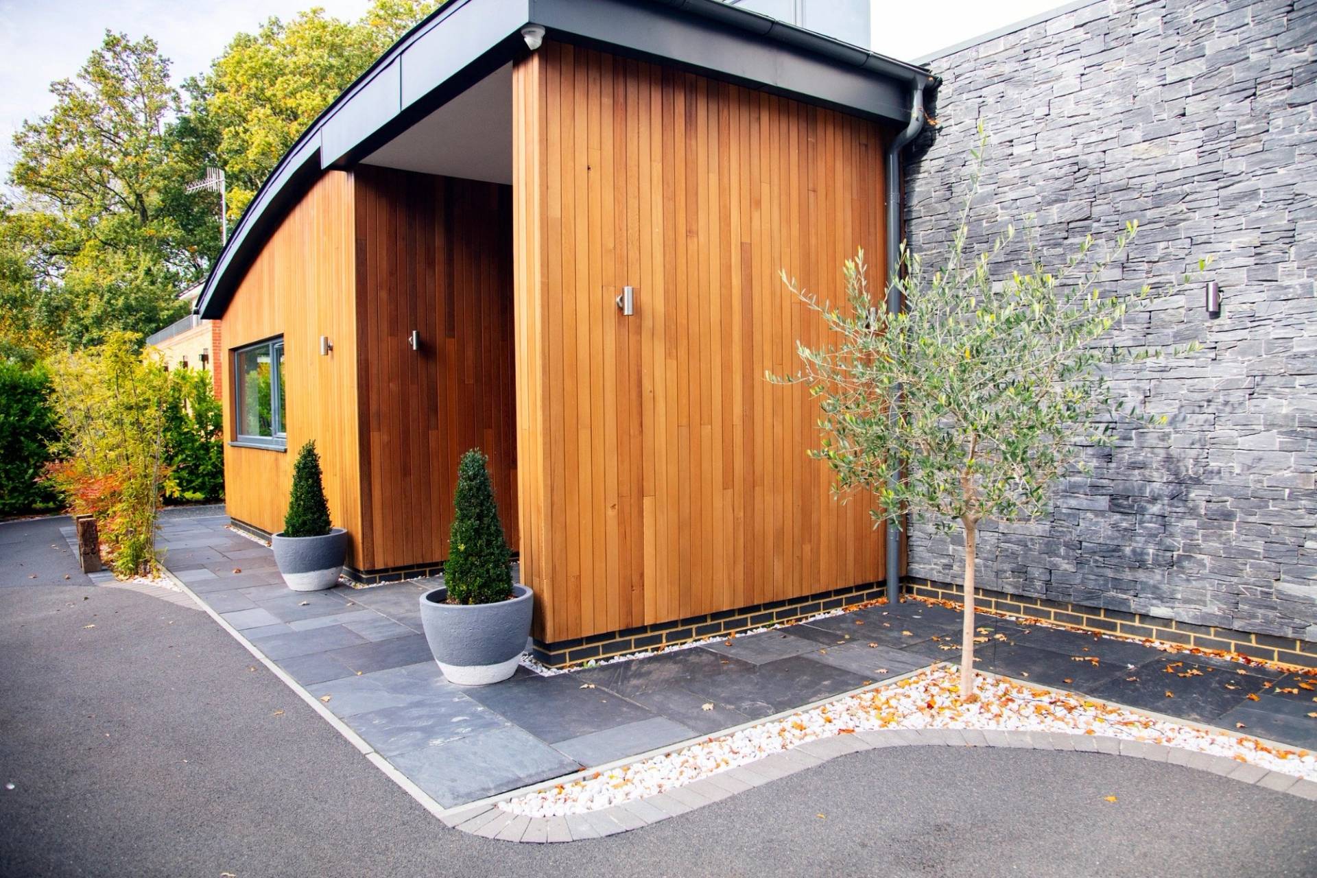 Close-up crop of a curved cedar wood entryway facade with warm external up-lighting accents, listed on Love Locations Surrey.