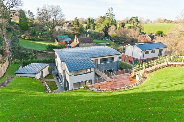 High-angle view of a modern timber-clad house facade nestled within beautifully landscaped rolling green hills, Love Locations.