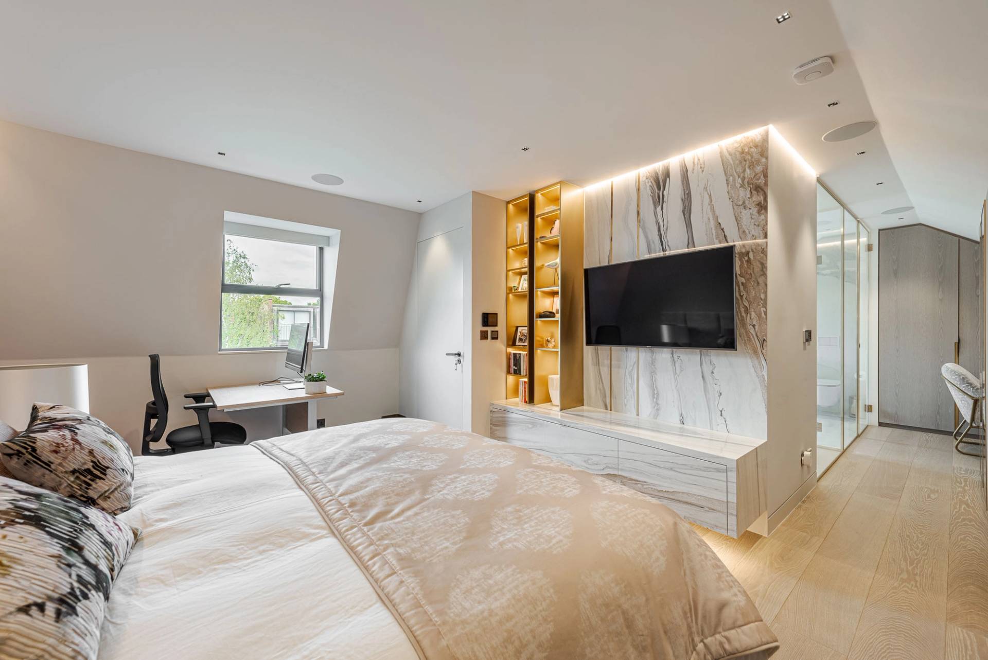 Bedroom suite featuring a white marble TV accent wall, gold built-in shelving, and neutral decor, Love Locations SW11.