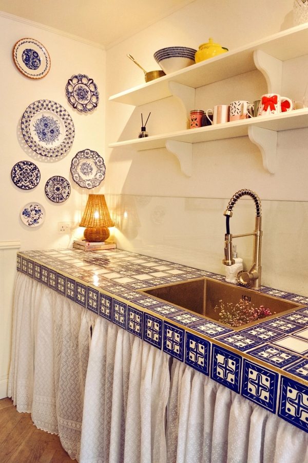Detailed shot of a blue-and-white tiled kitchen counter with open wooden shelving and brass fixtures, perfect for product and homeware advertising, Love Locations TW7.