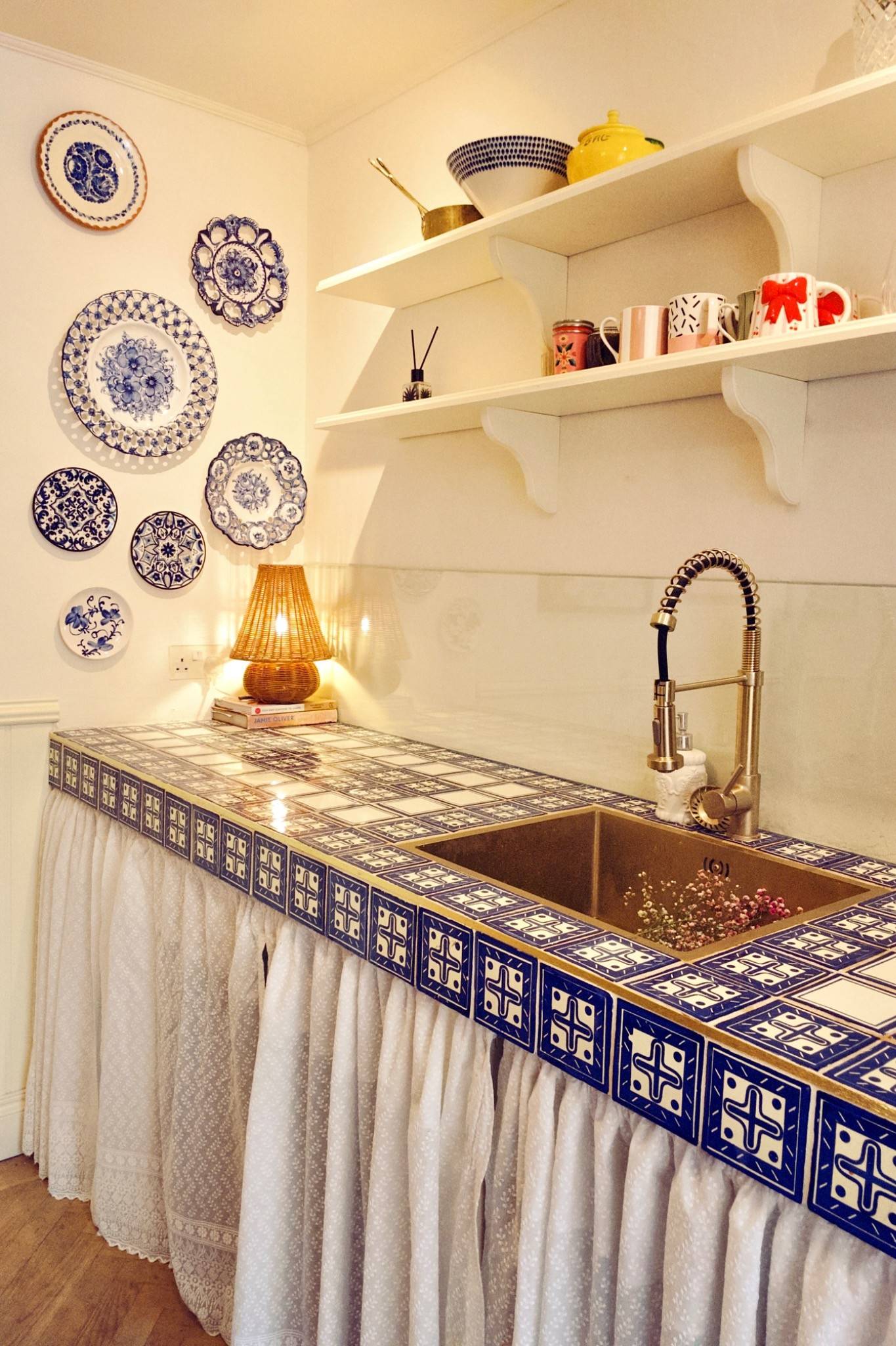 Detailed shot of a blue-and-white tiled kitchen counter with open wooden shelving and brass fixtures, perfect for product and homeware advertising, Love Locations TW7.