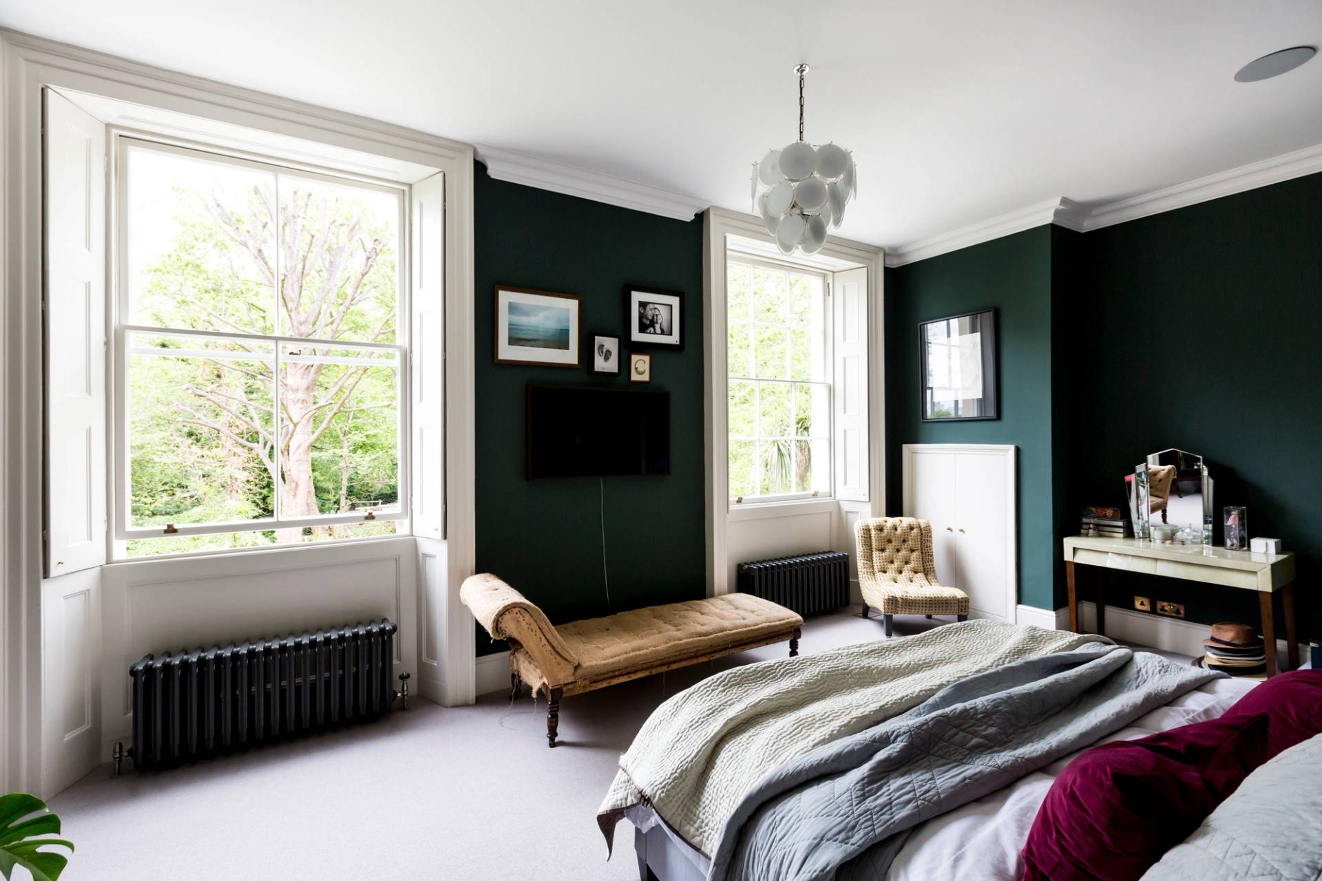 Dark green bedroom setup featuring a tan leather daybed, sash window, and black radiator in SE5 via Love Locations.
