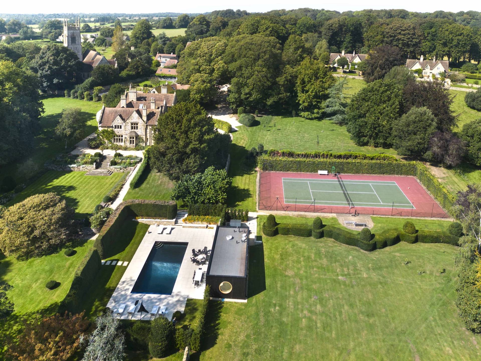 Aerial view of a luxury Cotswold country estate featuring a tennis court, swimming pool, and gardens, Love Locations OX7.