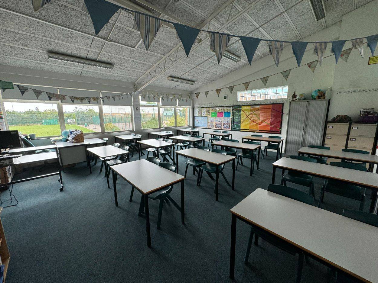 Bright school classroom filming location in North Finchley N12, featuring student desks, blue chairs, bunting, and large windows from Love Locations.