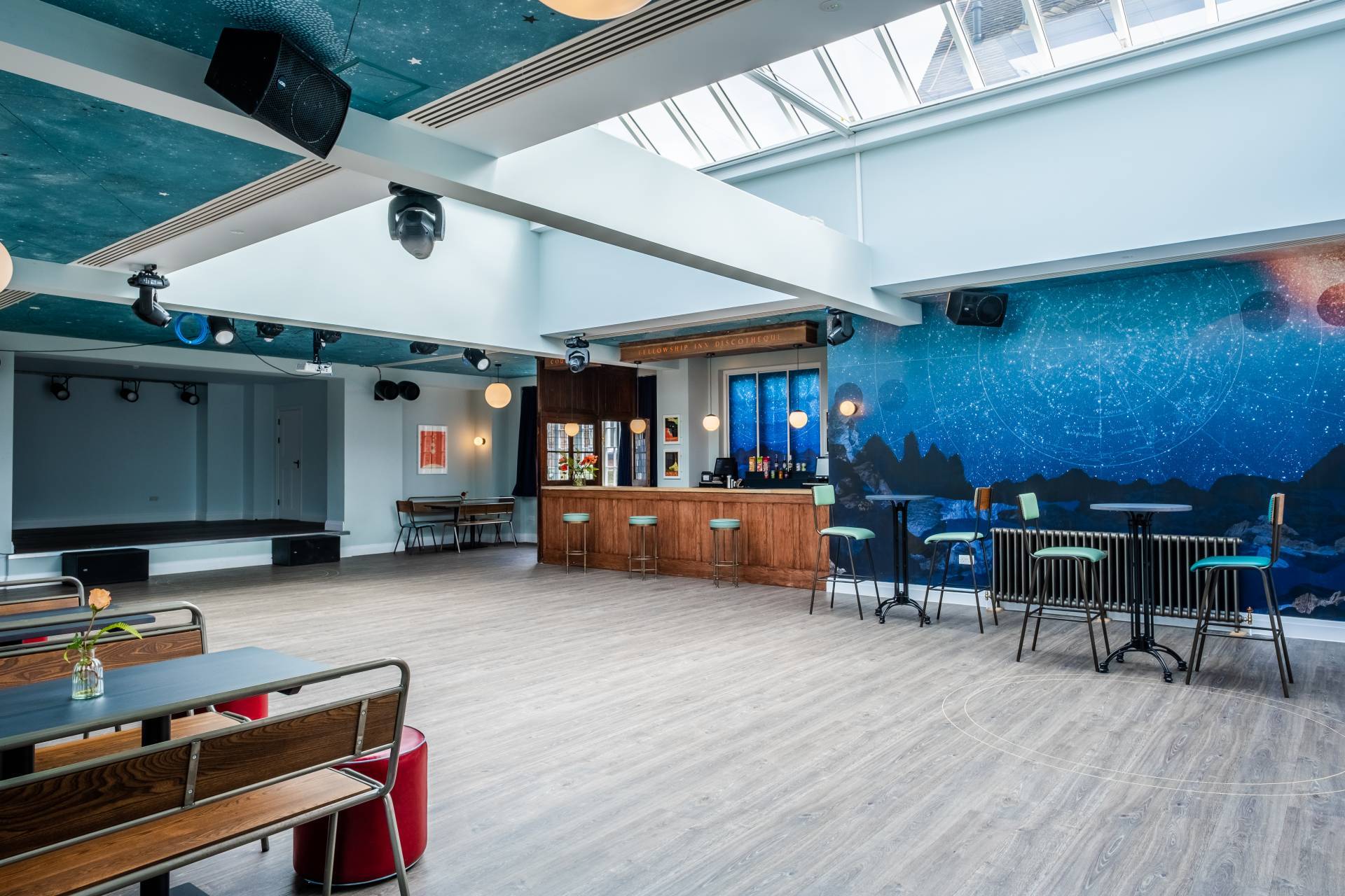 Sprawling open-plan event space and bar location in Lewisham SE6 from Love Locations, featuring light wood flooring, a central skylight, and a blue accent wall.