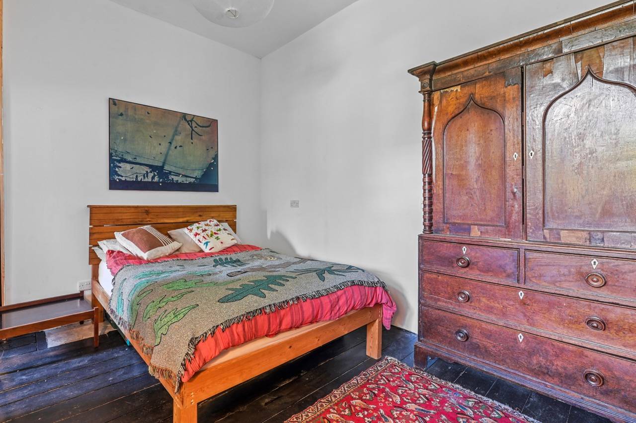 Guest bedroom featuring a timber bed frame, antique wooden wardrobe, and red patterned rug, Love Locations.