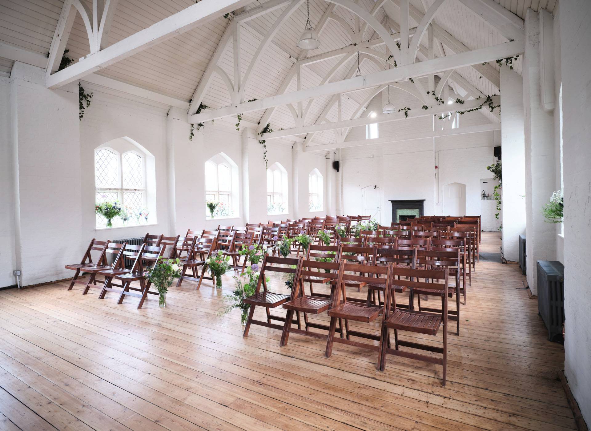 Wide-angle wedding layout in a white vaulted hall with timber floors and hanging botanical arrangements, perfect for bridal editorials, Love Locations.