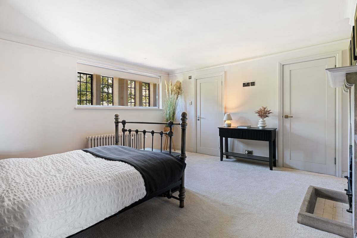 Guest bedroom with a dark metal bed frame, black decorative fireplace, and neutral carpets, Love Locations RH13.