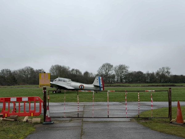 Historic airfield security entrance gate with warning signs and vintage aircraft in the background, great for dramatic narrative film sets, Love Locations.