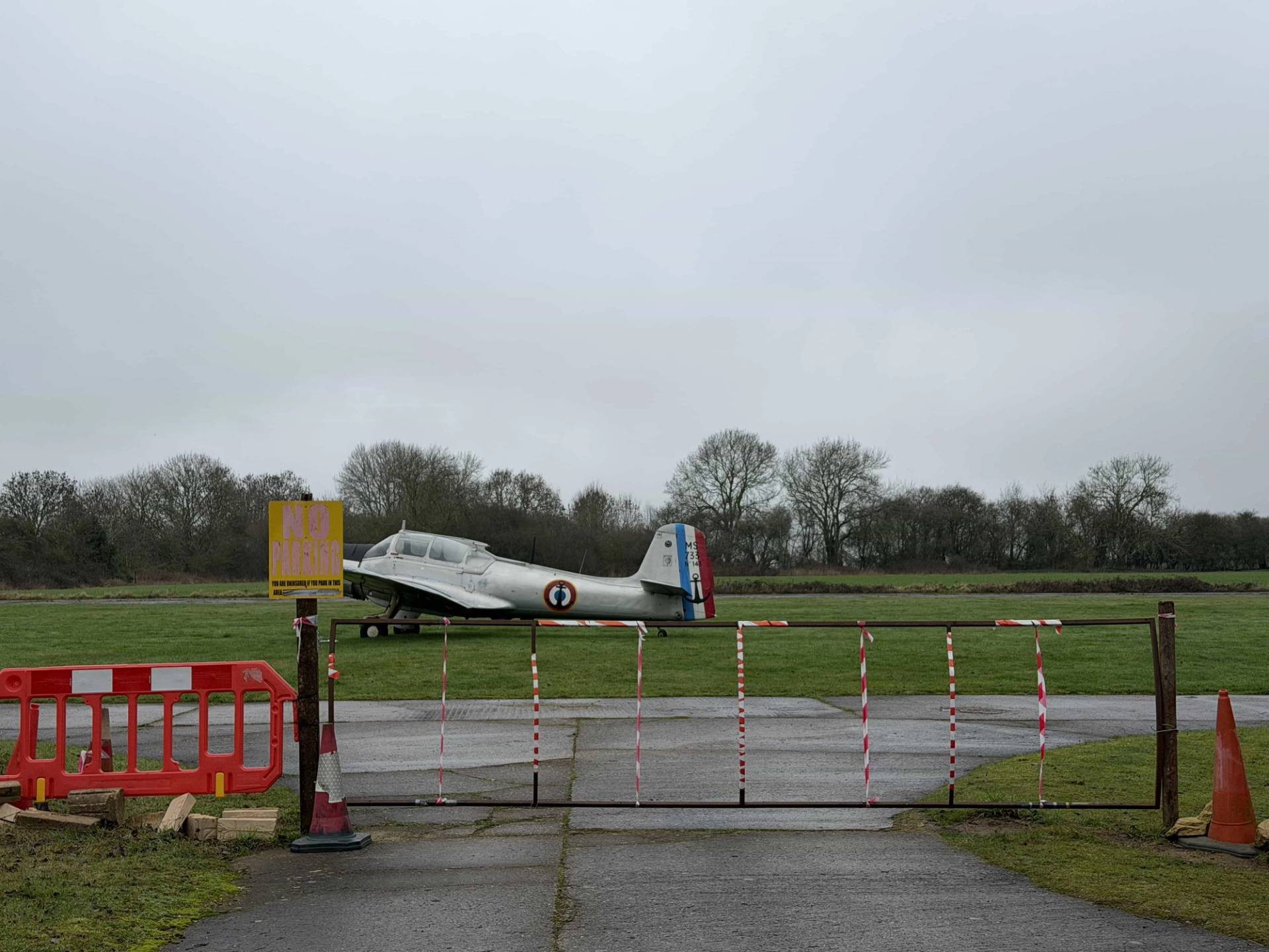 Historic airfield security entrance gate with warning signs and vintage aircraft in the background, great for dramatic narrative film sets, Love Locations.