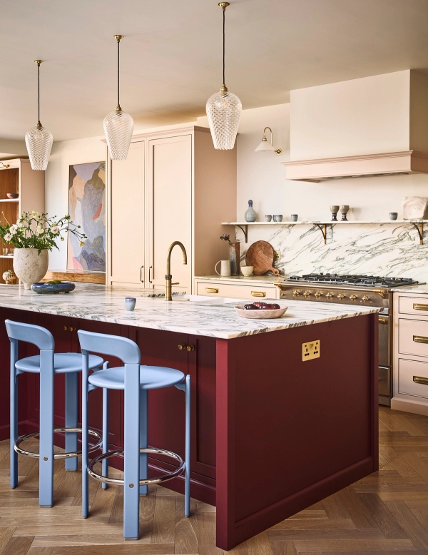 Luxury kitchen island featuring deep red cabinetry, white veined marble countertops, and blue bar stools, Love Locations SE21.
