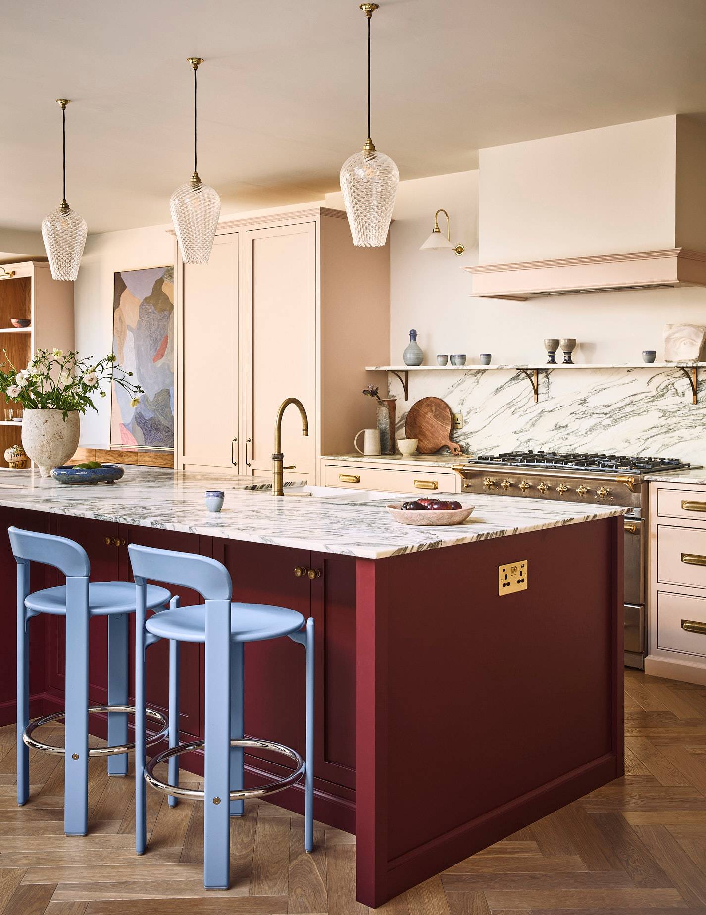 Luxury kitchen island featuring deep red cabinetry, white veined marble countertops, and blue bar stools, Love Locations SE21.