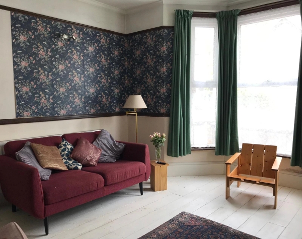 Vintage style double reception room in South London with a deep red sofa, patterned accent walls, and abundant natural light, perfect for independent film sets, Love Locations.