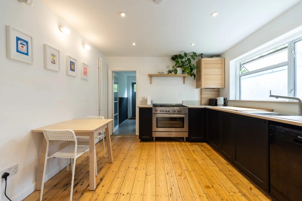 Love Locations Victorian terrace house shoot location Forest Gate E7: Modern kitchen with black cabinets, stripped wooden floors, a large steel range cooker, and breakfast table, ideal for lifestyle shoots and food commercials.