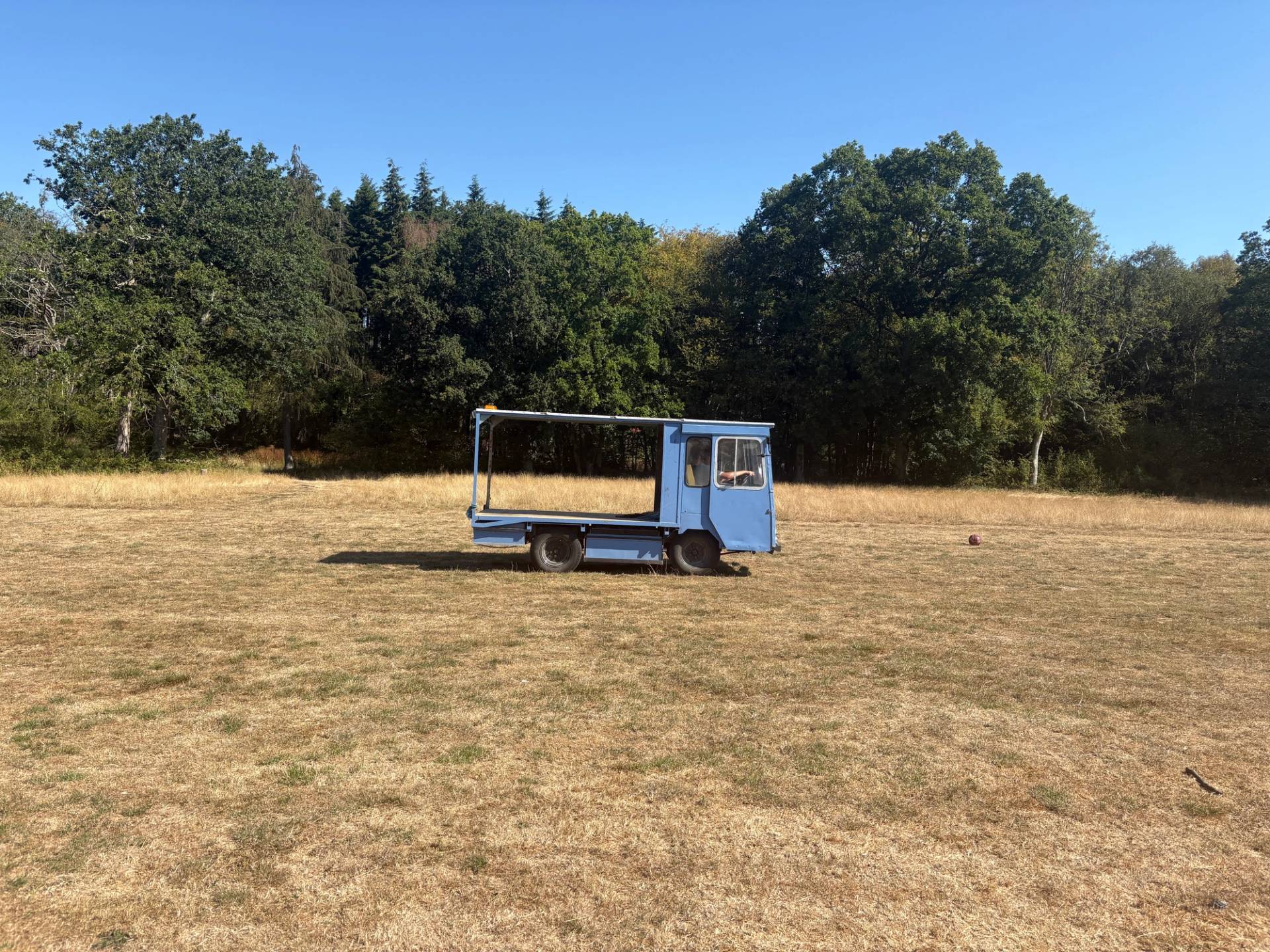 Blue flatbed utility trailer vehicle parked in a dry grassy meadow field, Love Locations BN8.