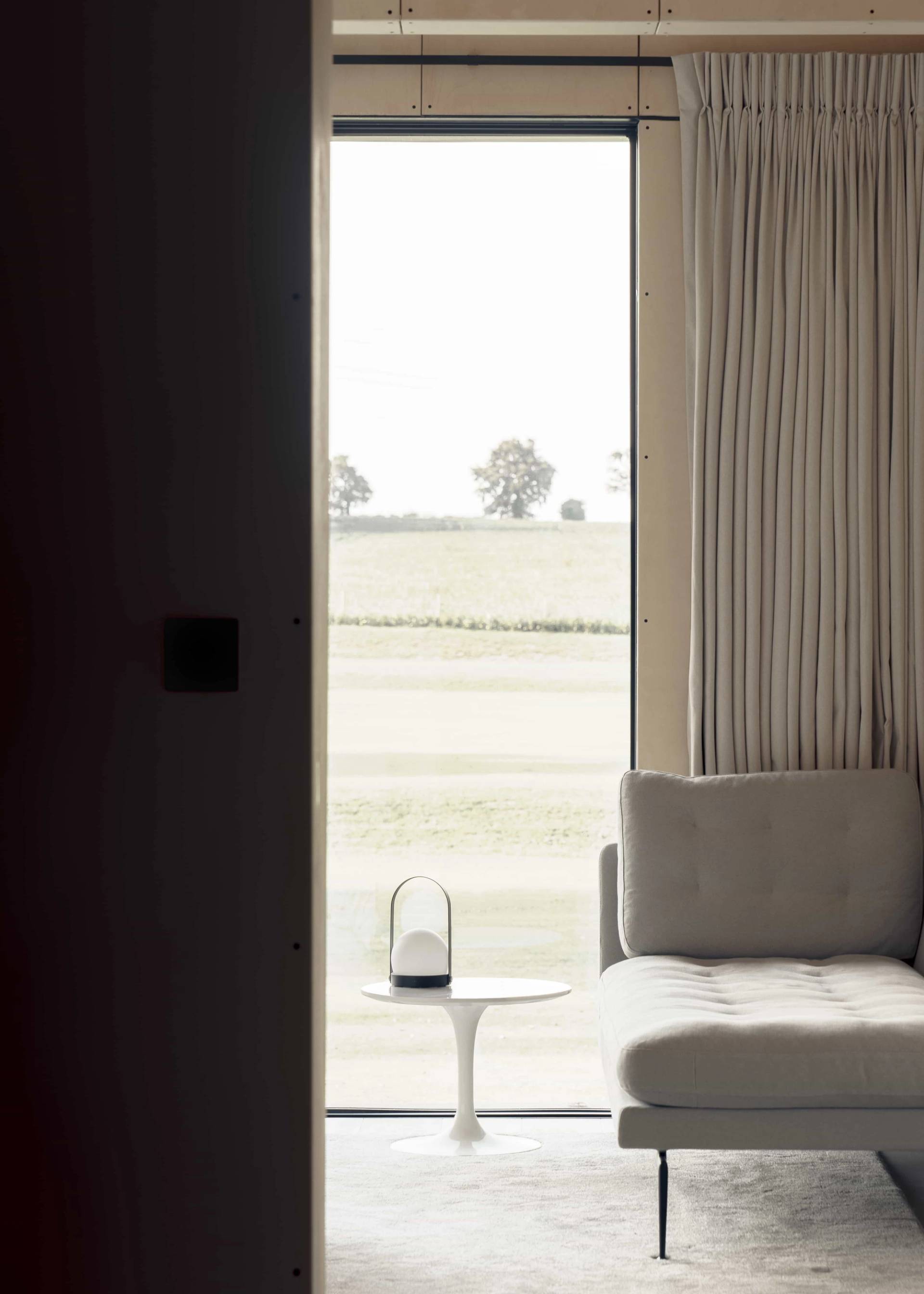 Serene bedroom nook featuring a low cream armchair, white side table, and full-height window overlooking Norfolk fields, Love Locations NR9.