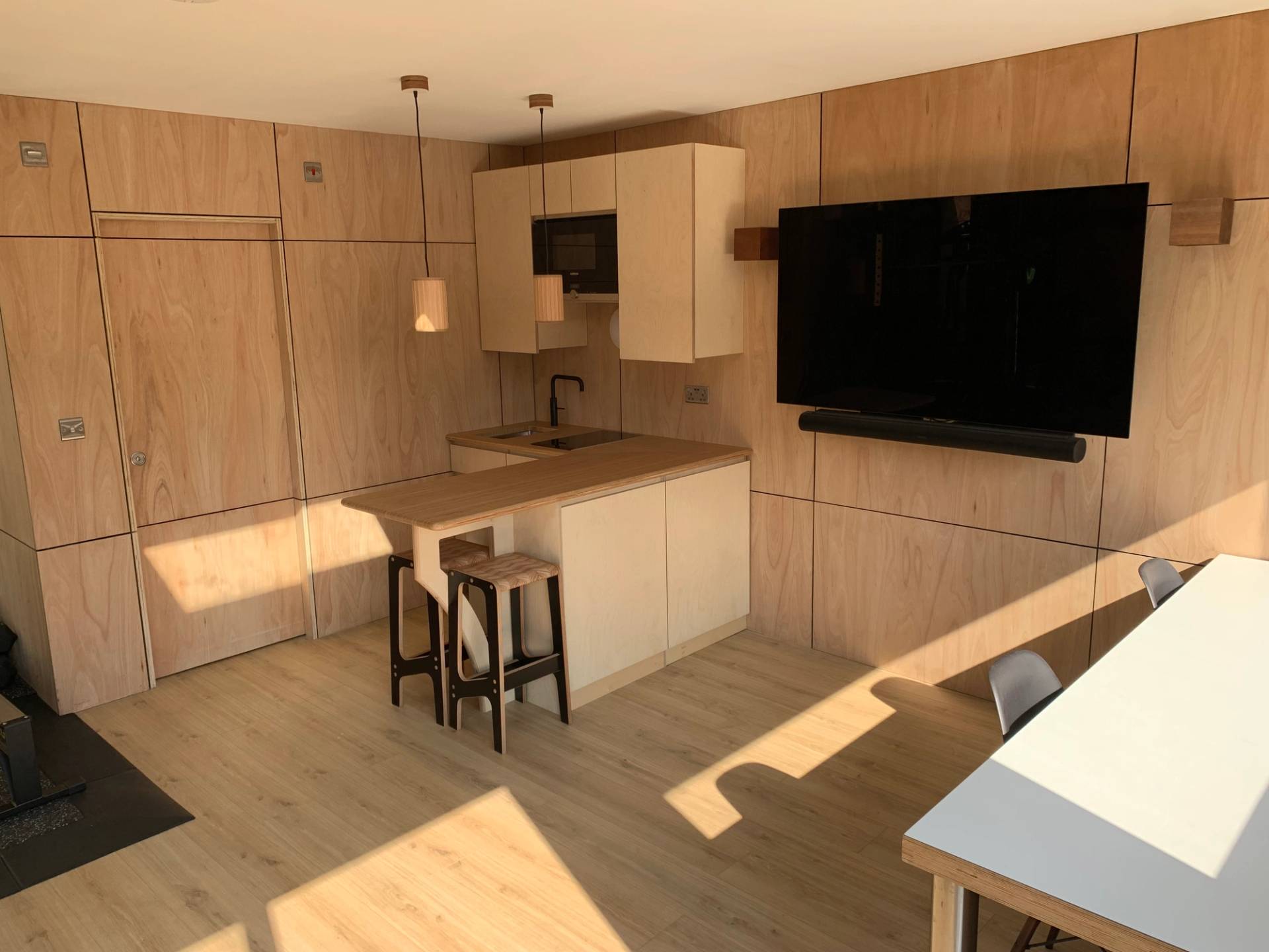Plywood panelled home gym outbuilding interior featuring a wooden counter and black bar stools, Love Locations TW1.