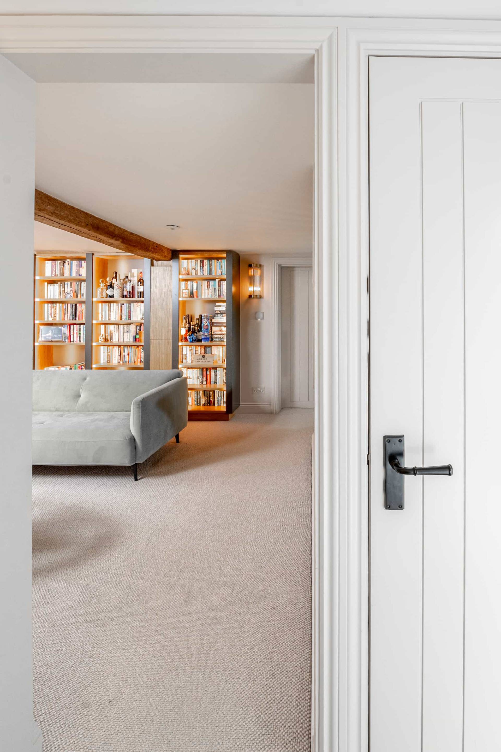 View looking through a white painted panelled doorway into a cozy living room with bookshelf storage, Love Locations GU28.