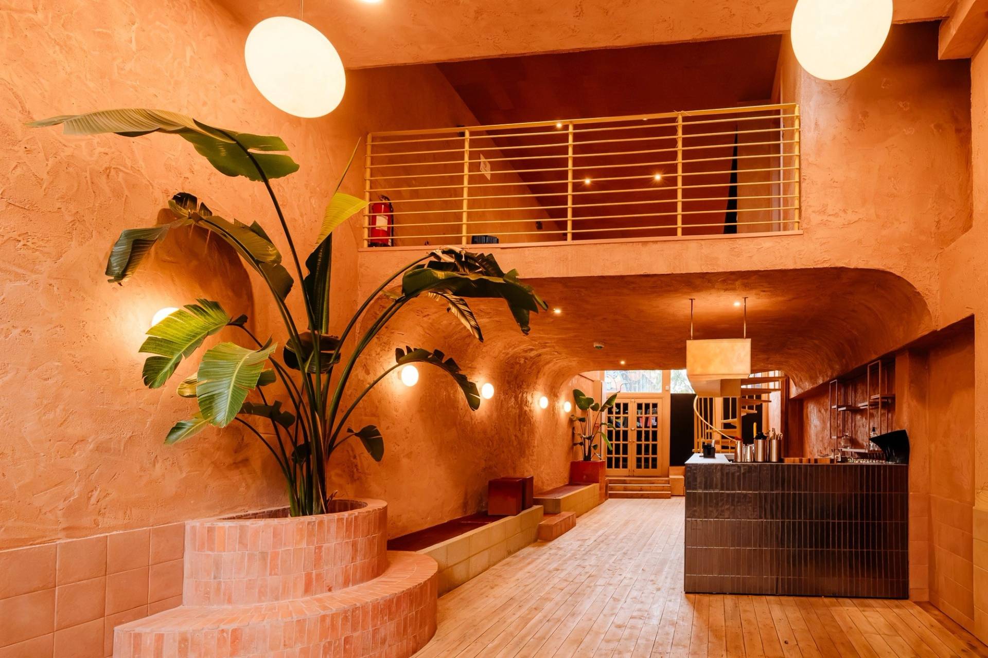 Warm terracotta textured lounge and bar venue in Hackney EC2A from Love Locations, featuring a mezzanine level, built-in bench seating, and indoor tropical plants.