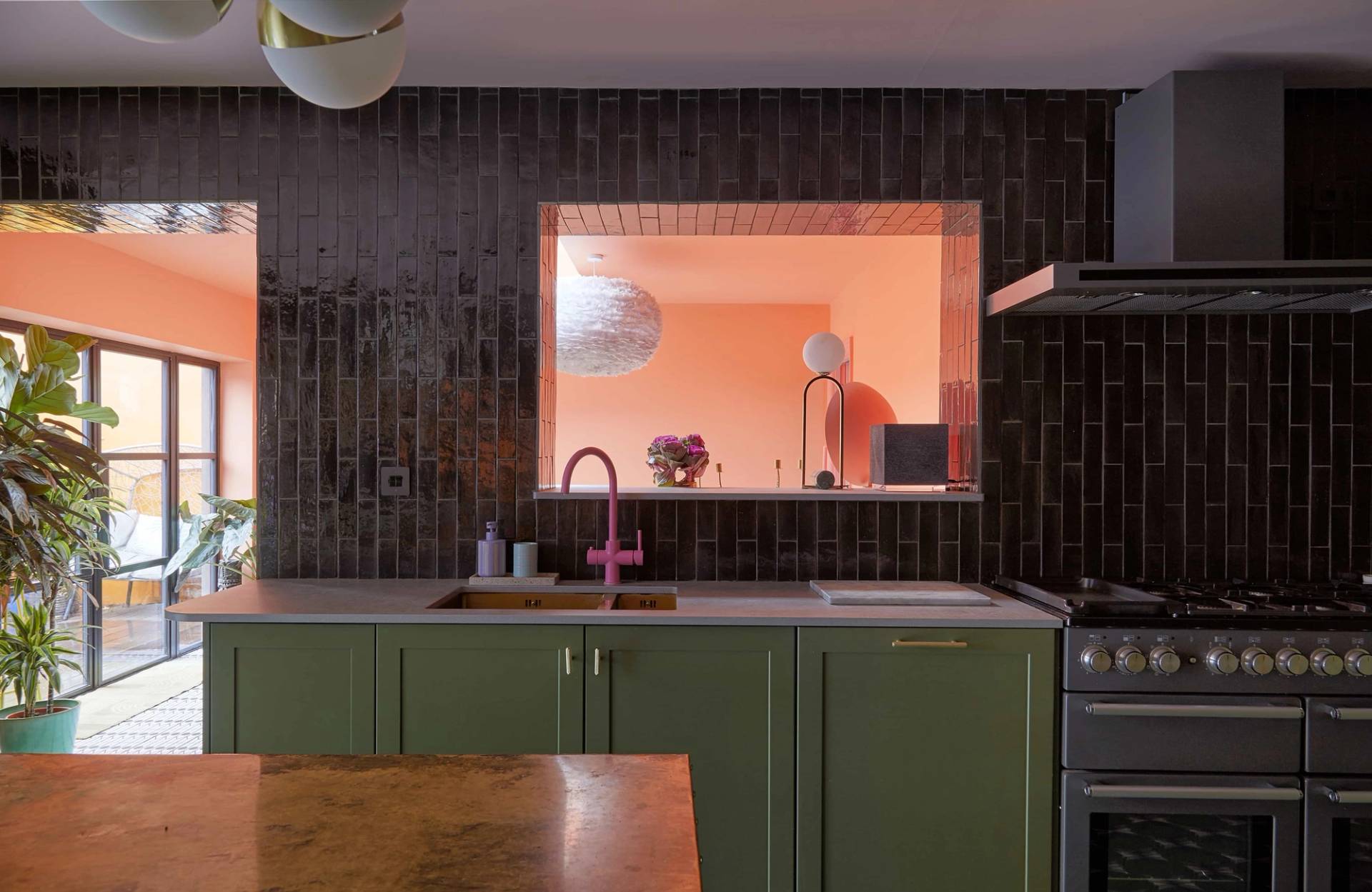 Internal cutout window view looking from an olive green kitchen into a bright coral orange dining space, Love Locations Catford.