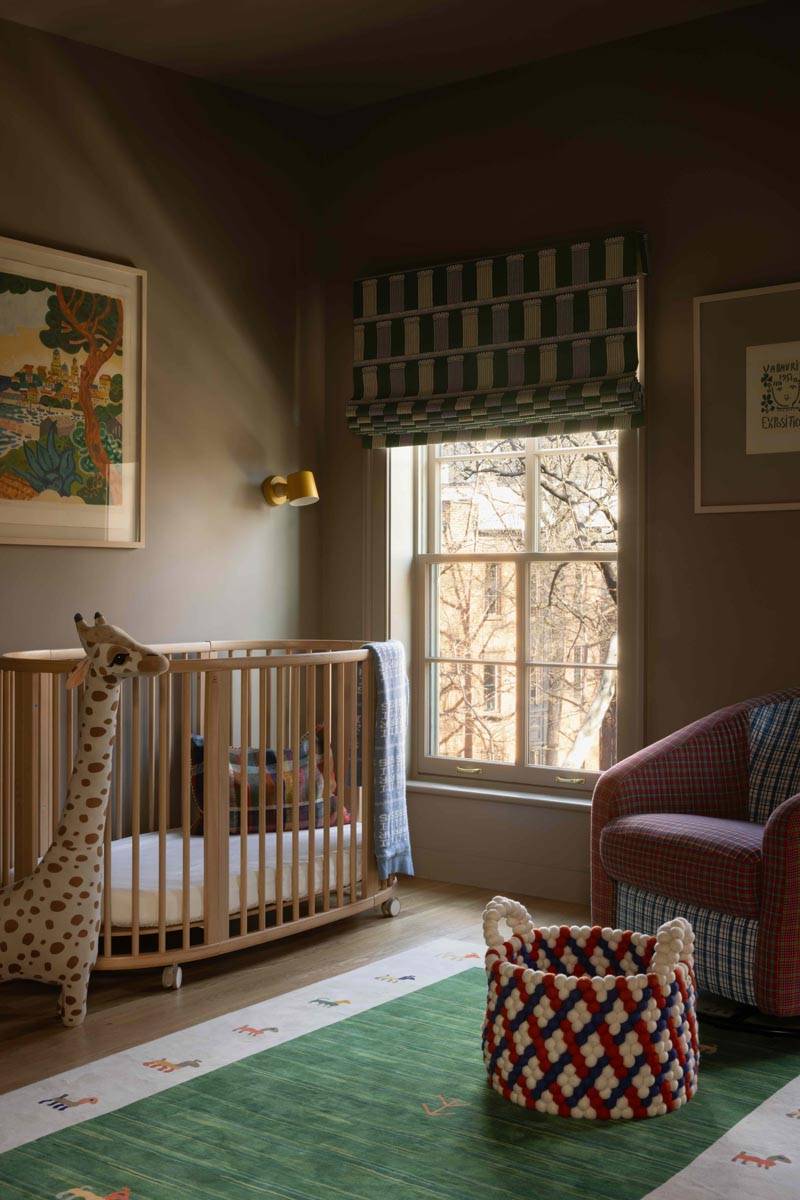 Cozy nursery location house in Boerum Hill Brooklyn by Love Locations, featuring a wooden crib, geometric patterned rug, and a tall giraffe plush toy by a sash window.