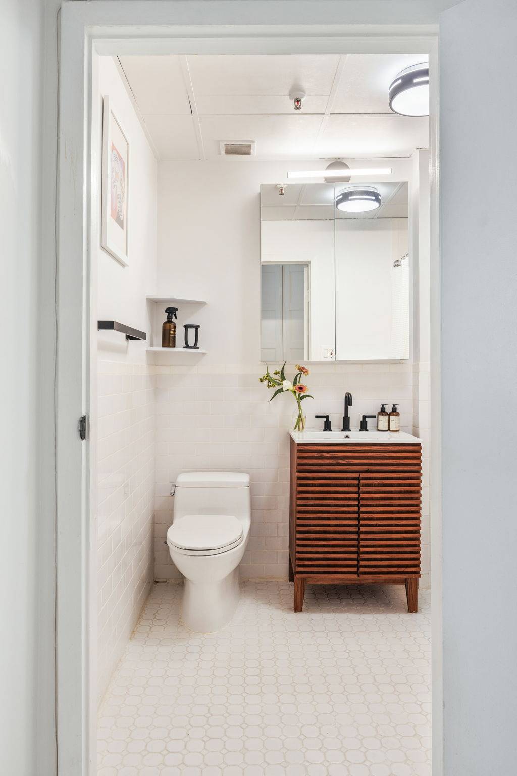 Modern vanity bathroom location featuring a slatted dark wood vanity cabinet, white subway tile, and mirror in a Tribeca loft via Love Locations.