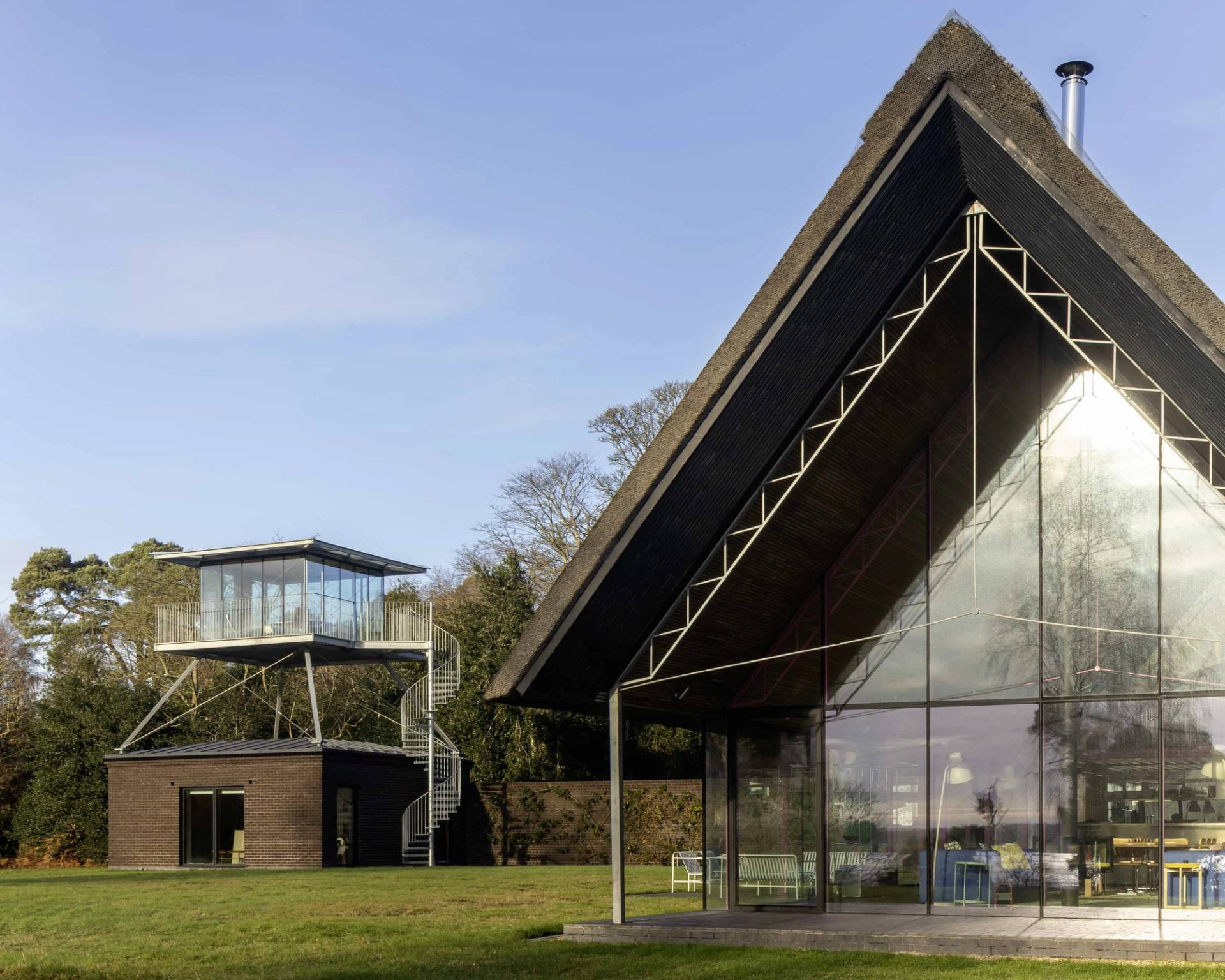 Contemporary glass longhouse set against open green lawns and surrounding native woodland, Love Locations IP17.