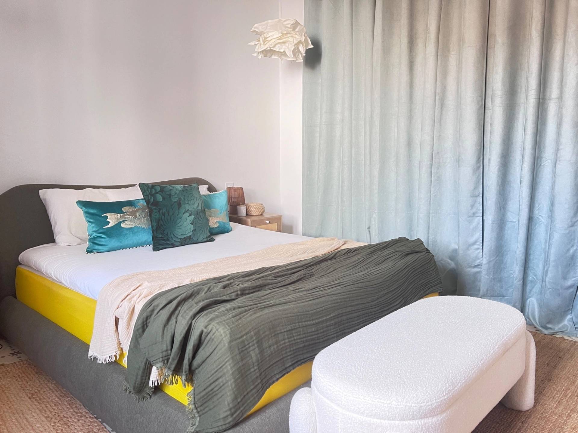Cozy bedroom photoshoot backdrop in Jimena de la Frontera through Love Locations, with green linen bedding, soft blue curtains, and a white upholstered bed end bench.
