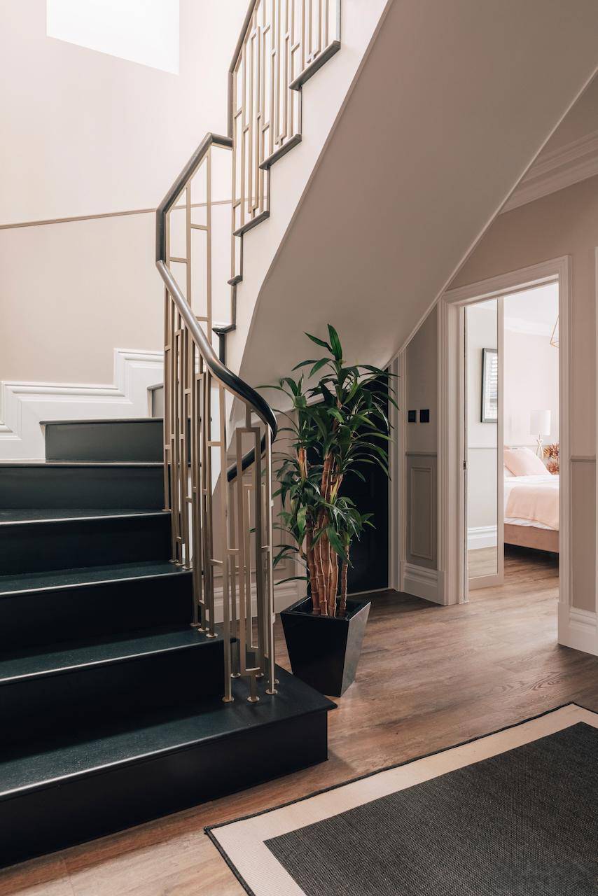 Grand entrance hall view looking up a black metal-balustrade staircase with indoor greenery, Love Locations W5.