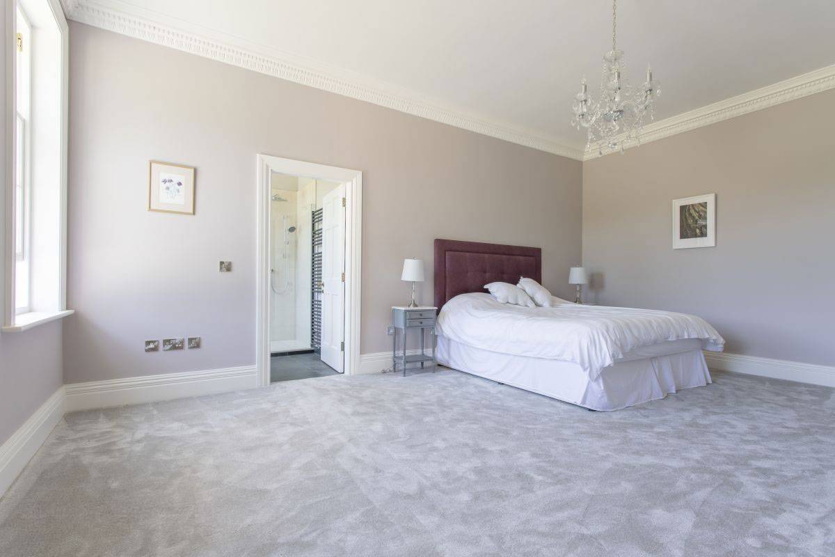 Sophisticated grey bedroom with a rich plum headboard and minimalist decor for TV and film shoots, curated by Love Locations.