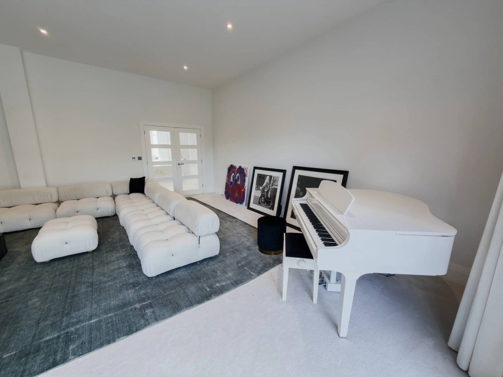 White grand piano and modular lounge seating setup inside a modern luxury residence in Barnet EN4 via Love Locations.