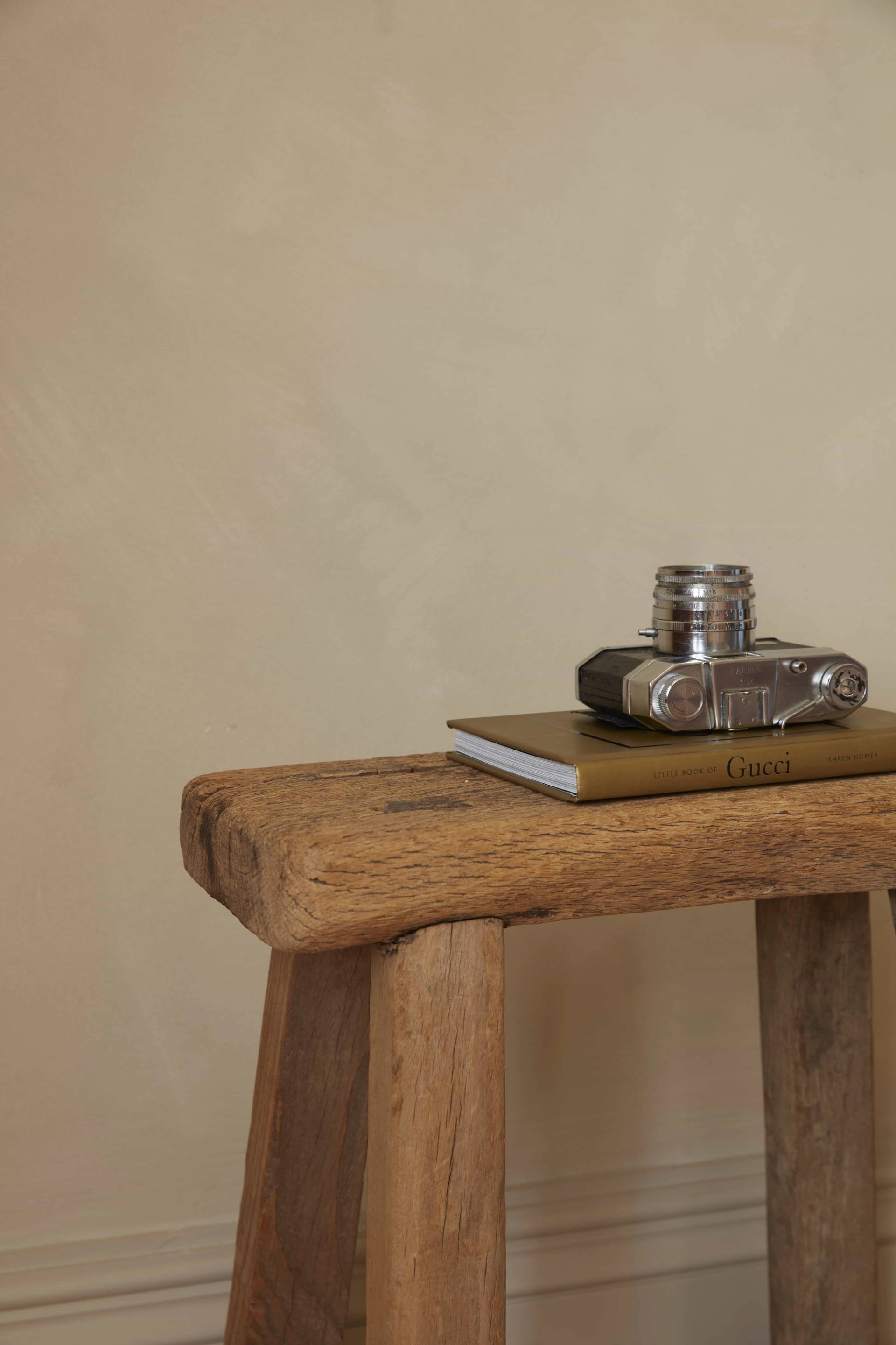 Rustic wooden stool with a vintage camera resting on plaster wall backdrops, ideal for product photography, Love Locations.