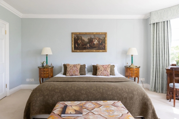 Love Locations boutique master bedroom Steyning: Symmetry-focused double bedroom with a muted duck-egg blue feature wall, brown quilted coverlet, and antique side tables, perfect for bedding shoots.