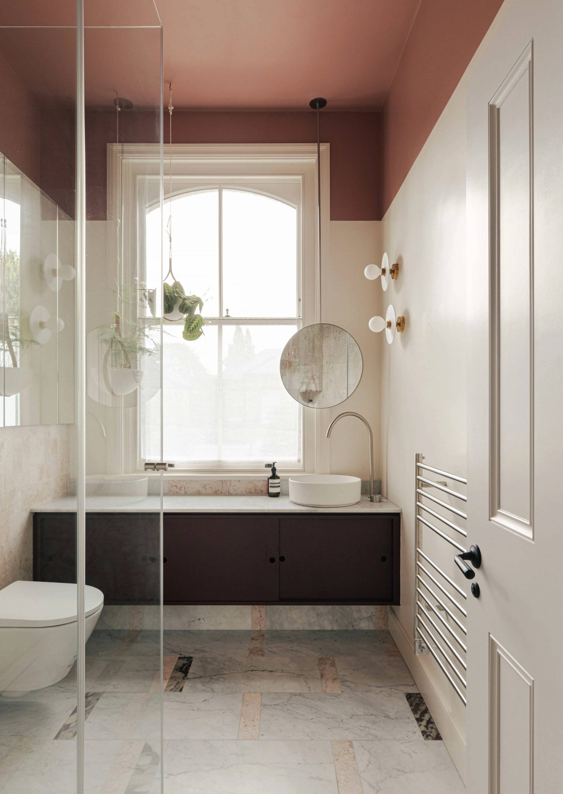 Guest bathroom featuring a dark wood vanity sink, white sash window, and terracotta pink upper walls, Love Locations.