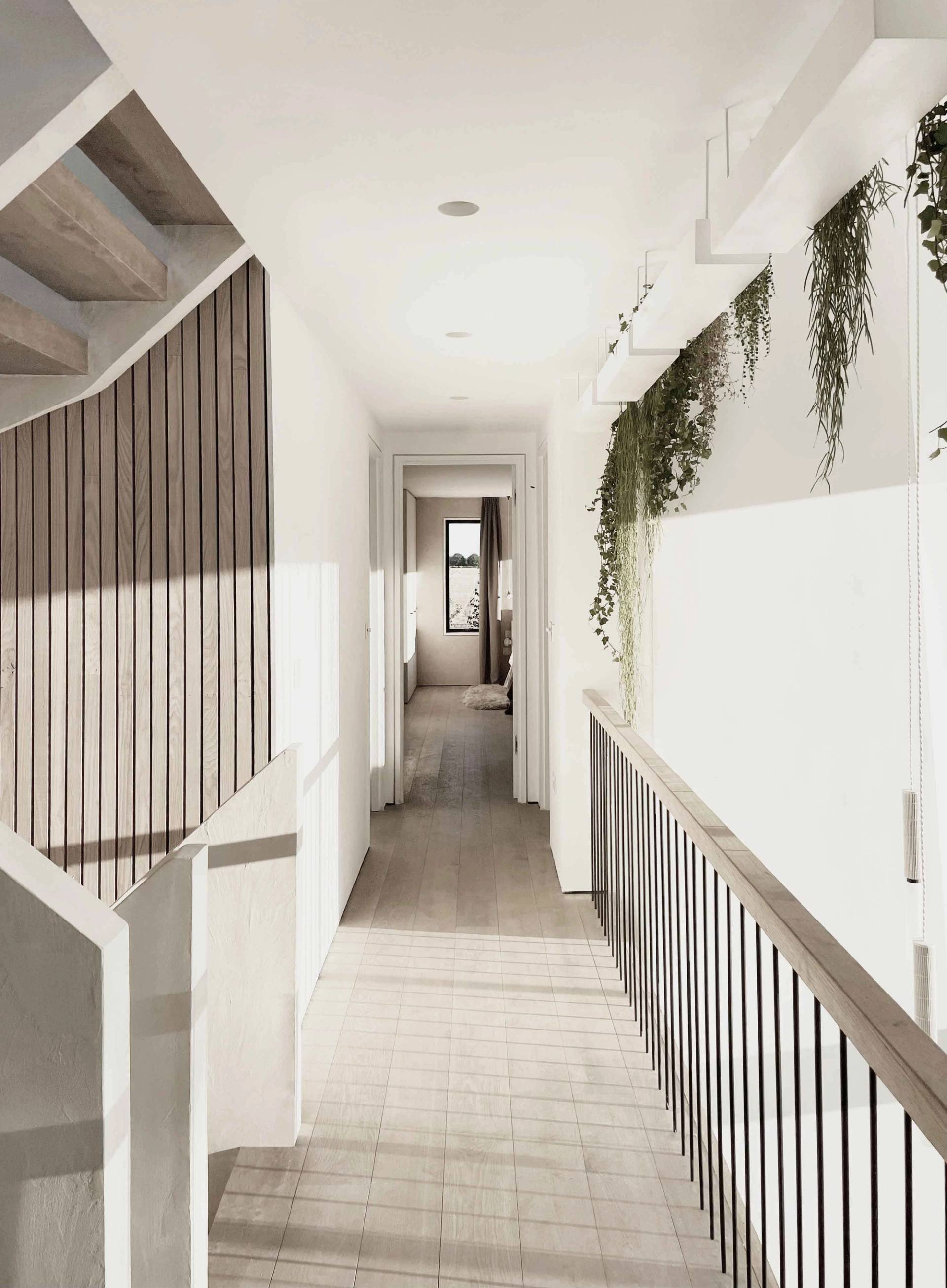 Upper mezzanine corridor with a wooden balustrade, trailing greenery, and light wood flooring in a Chichester eco-home, Love Locations PO18.