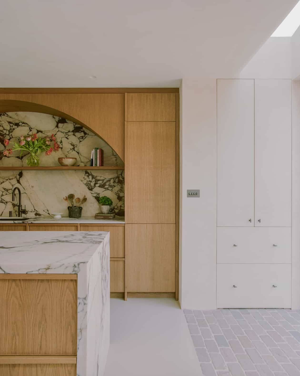 Seamless kitchen joinery with white integrated cabinets, oak arch display, and marble island counter, Love Locations SW4.