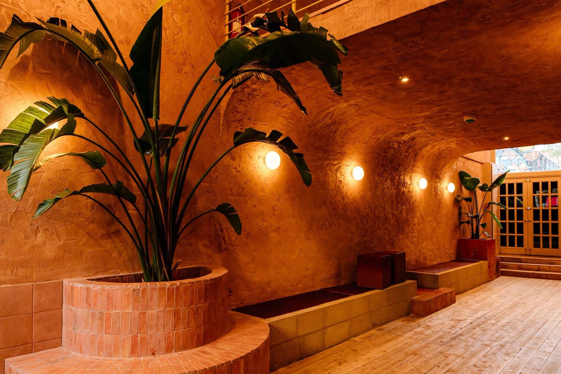 Close-up of a terracotta plaster seating alcove with ambient round wall sconces and lush indoor greenery in a Hackney location house from Love Locations.