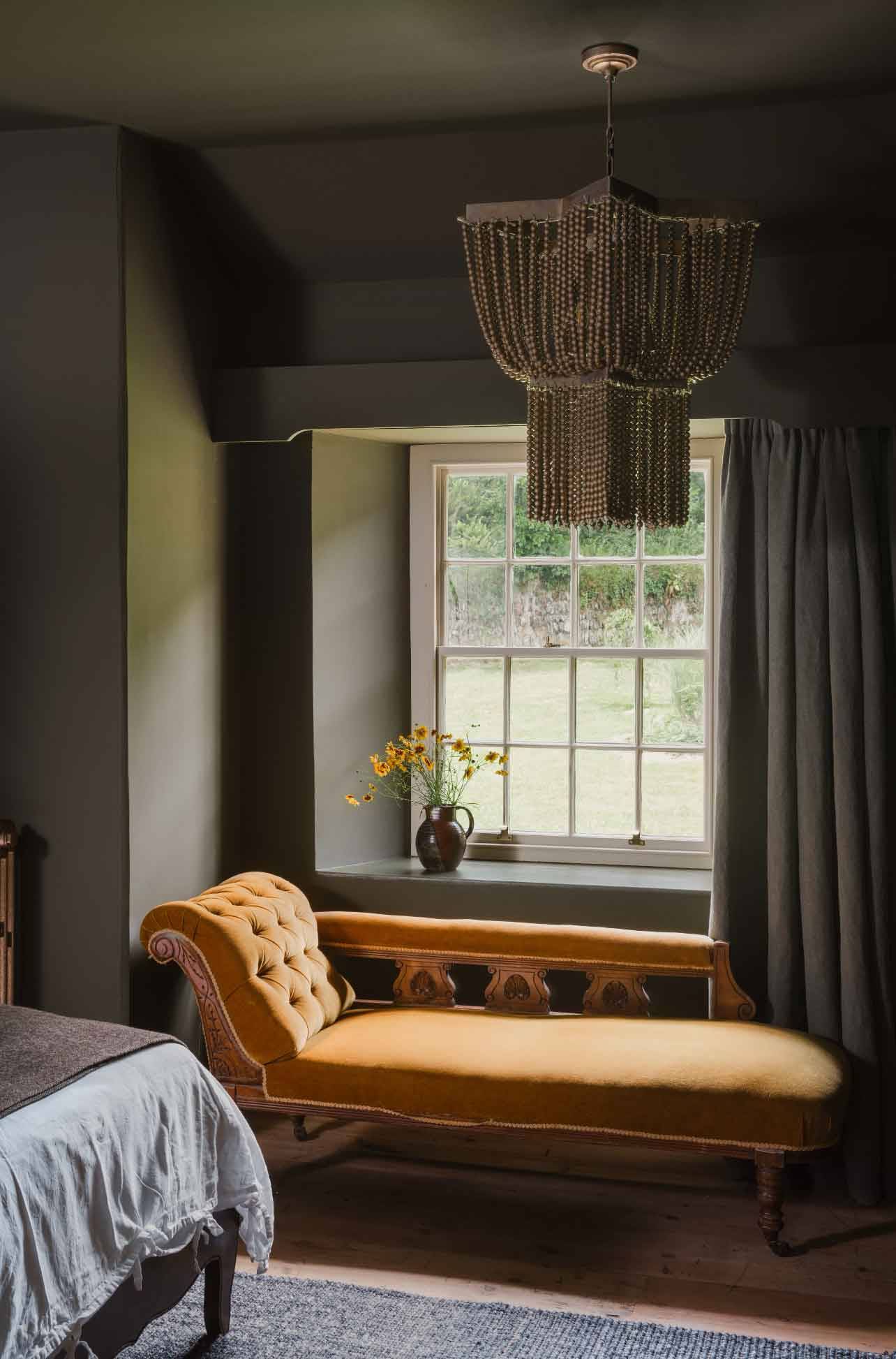 Mustard yellow chaise lounge by a sash window in a dark green bedroom film location through Love Locations.