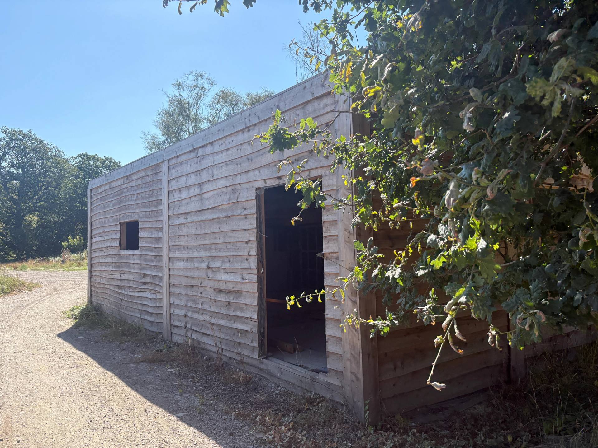 Rustic wooden timber cladding building exterior with open doorway set beside trees on farm grounds, Love Locations BN8.