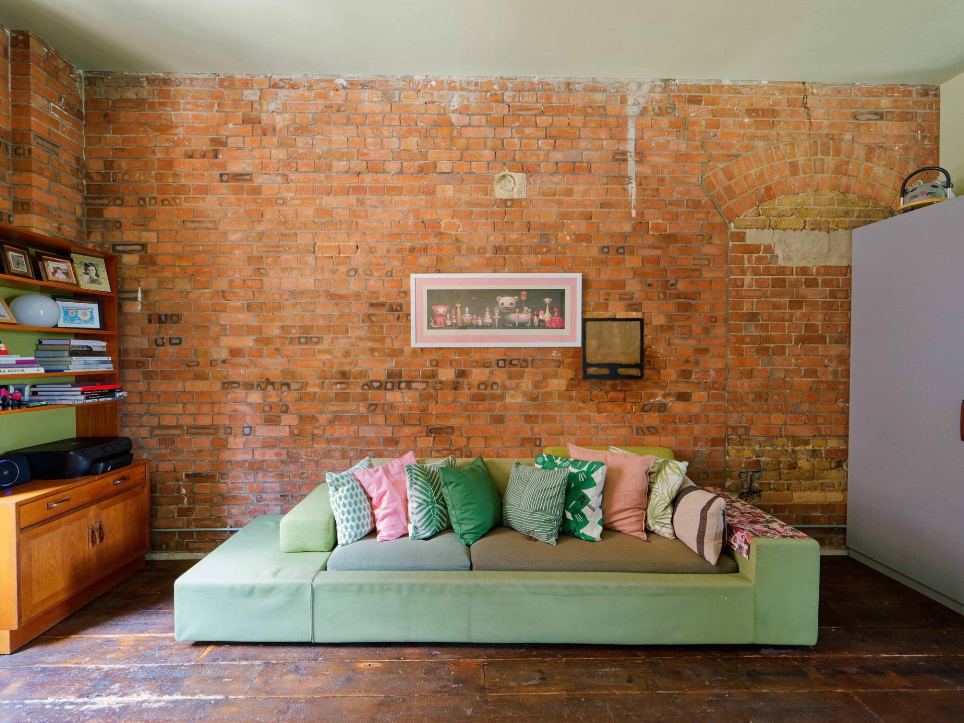 Exposed red brick wall backdrop styled with a low green bench sofa and plush throw cushions, perfect for product photography, Love Locations.