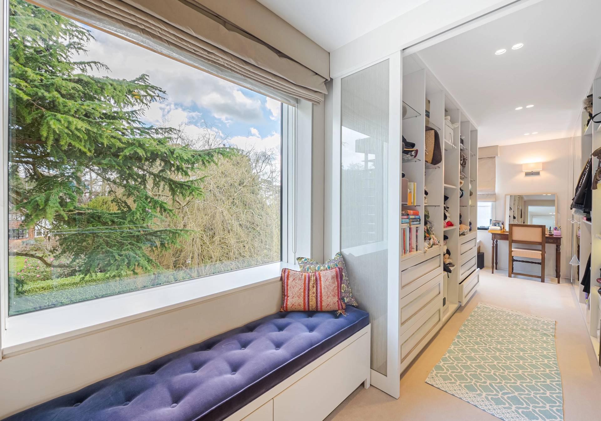 Fitted walk-in dressing room nook with a purple velvet window seat and tree canopy views, ideal for fashion accessories ads, Love Locations KT2.