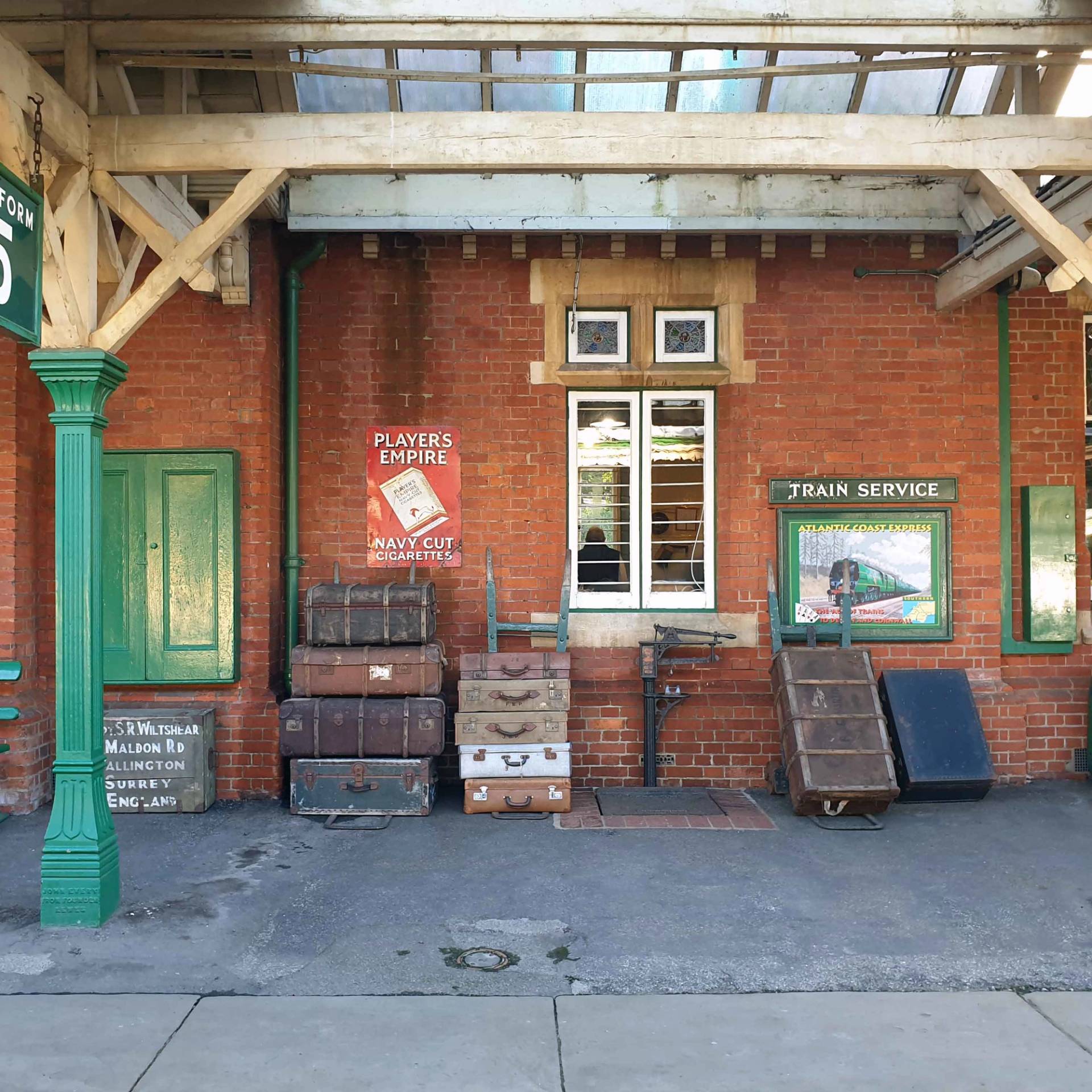 Heritage station platform display with vintage leather trunks, luggage carts, and brick building facade, Love Locations TN22 3QL.