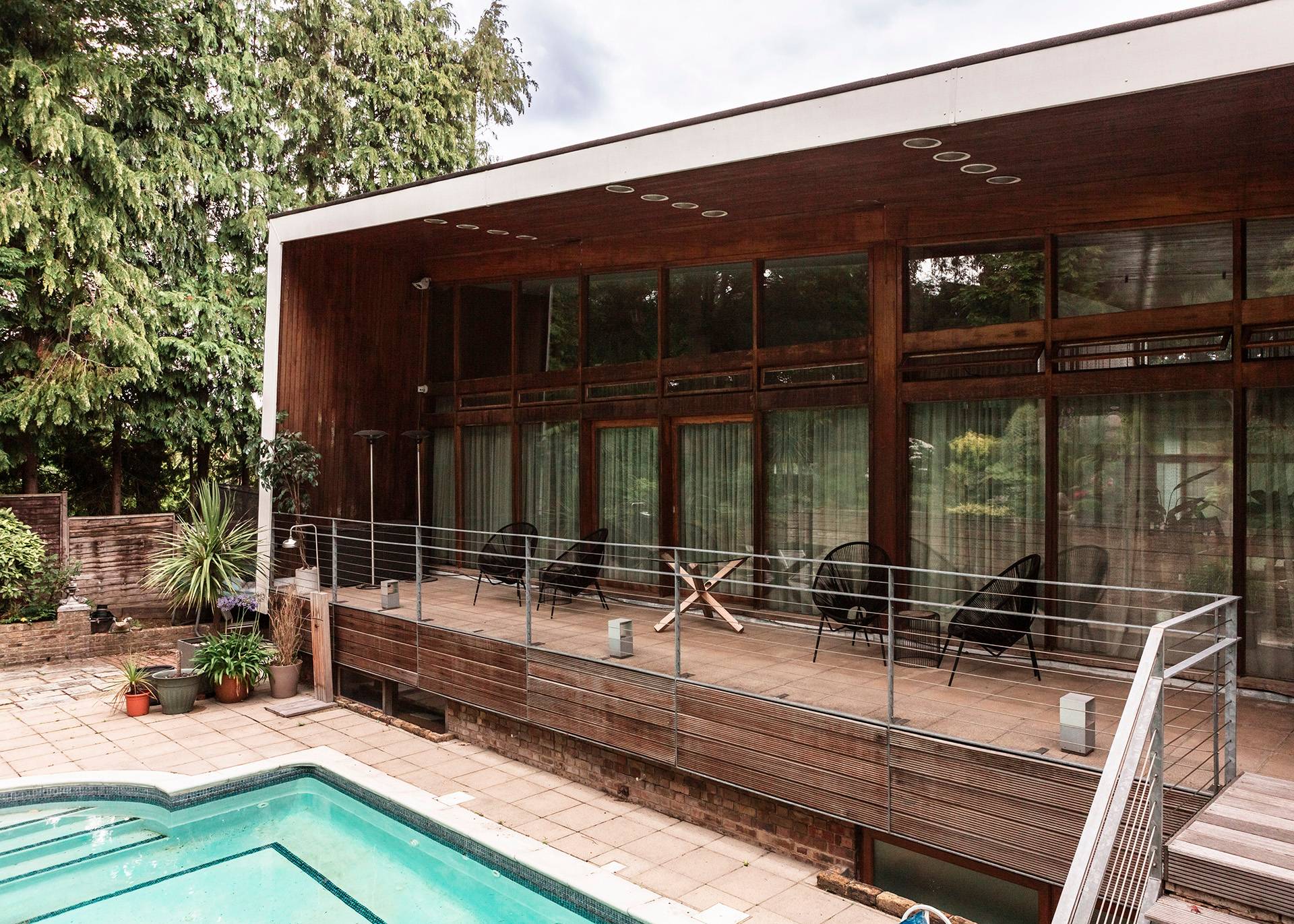 Elevated rear terrace deck of a mid-century architectural home overlooking a blue swimming pool and mature garden grounds, Love Locations BR1.